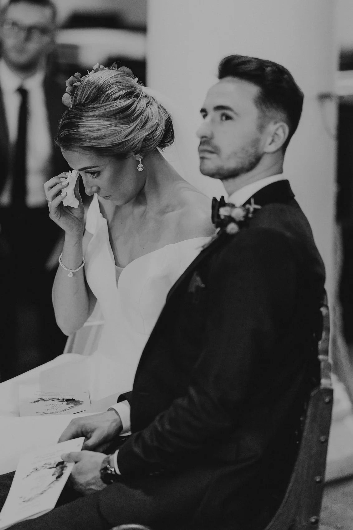 Black and white photo showing emotional wedding ceremony reactions during an intimate indoor service.