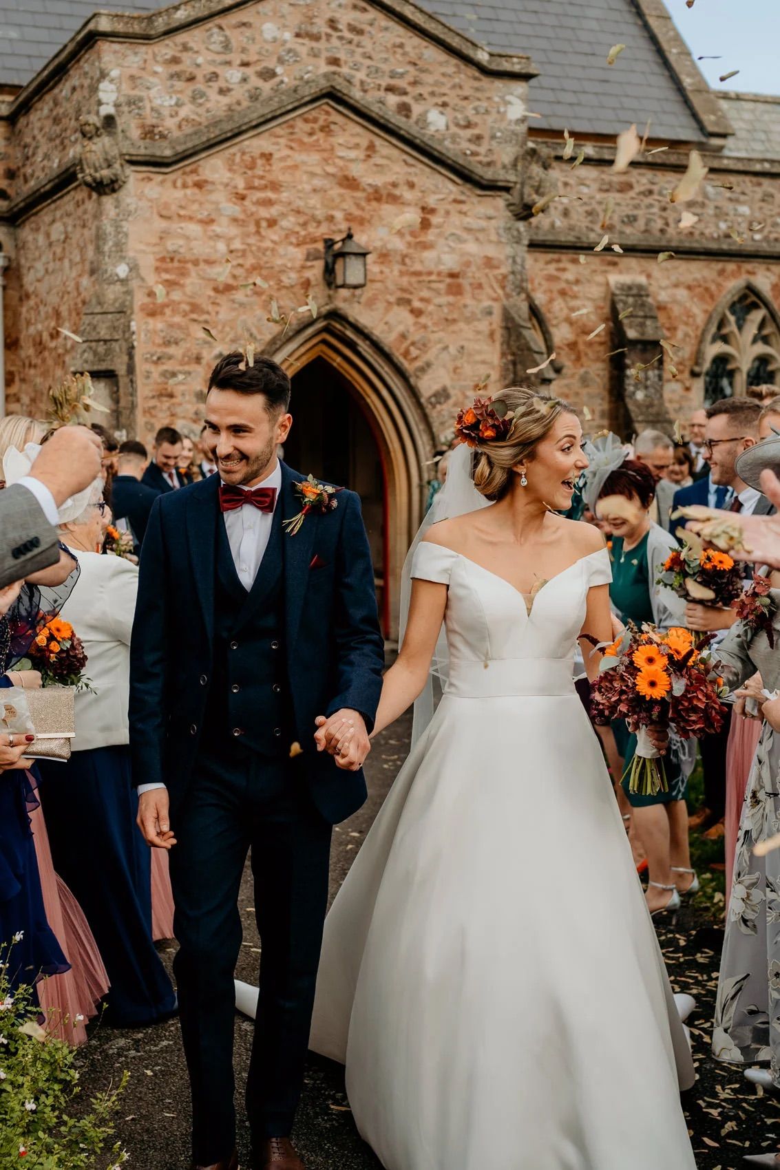 Newlyweds exit stone church while guests shower them with confetti on their wedding day.