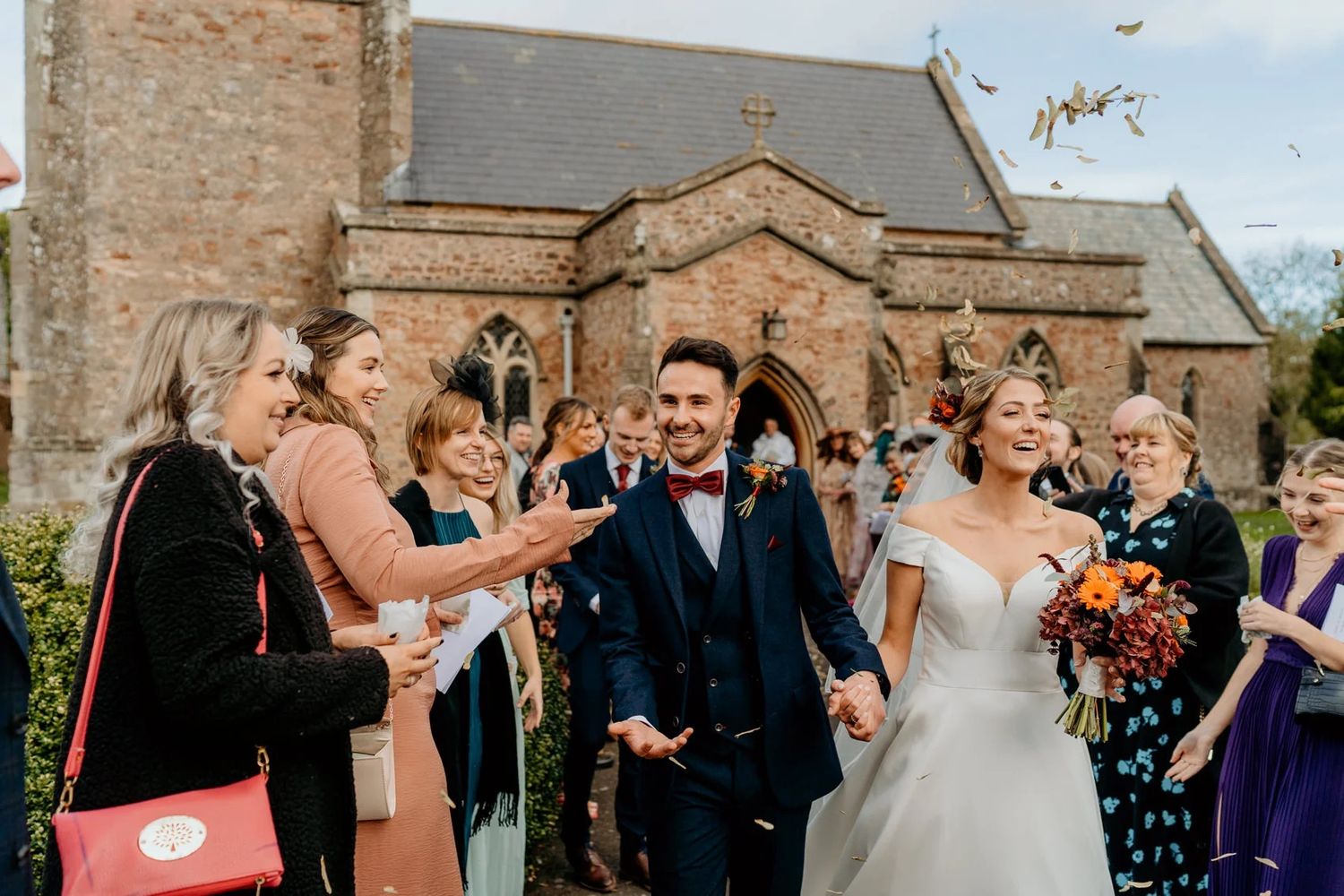 Wedding guests celebrate with confetti outside a historic stone church on a sunny day.