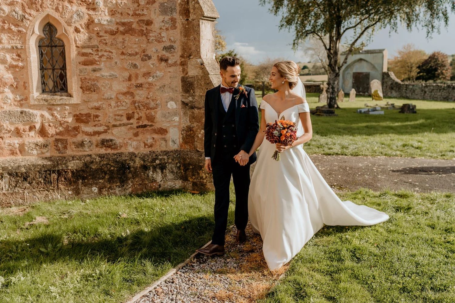 Rustic stone wall and autumn foliage create romantic backdrop for outdoor wedding portraits.