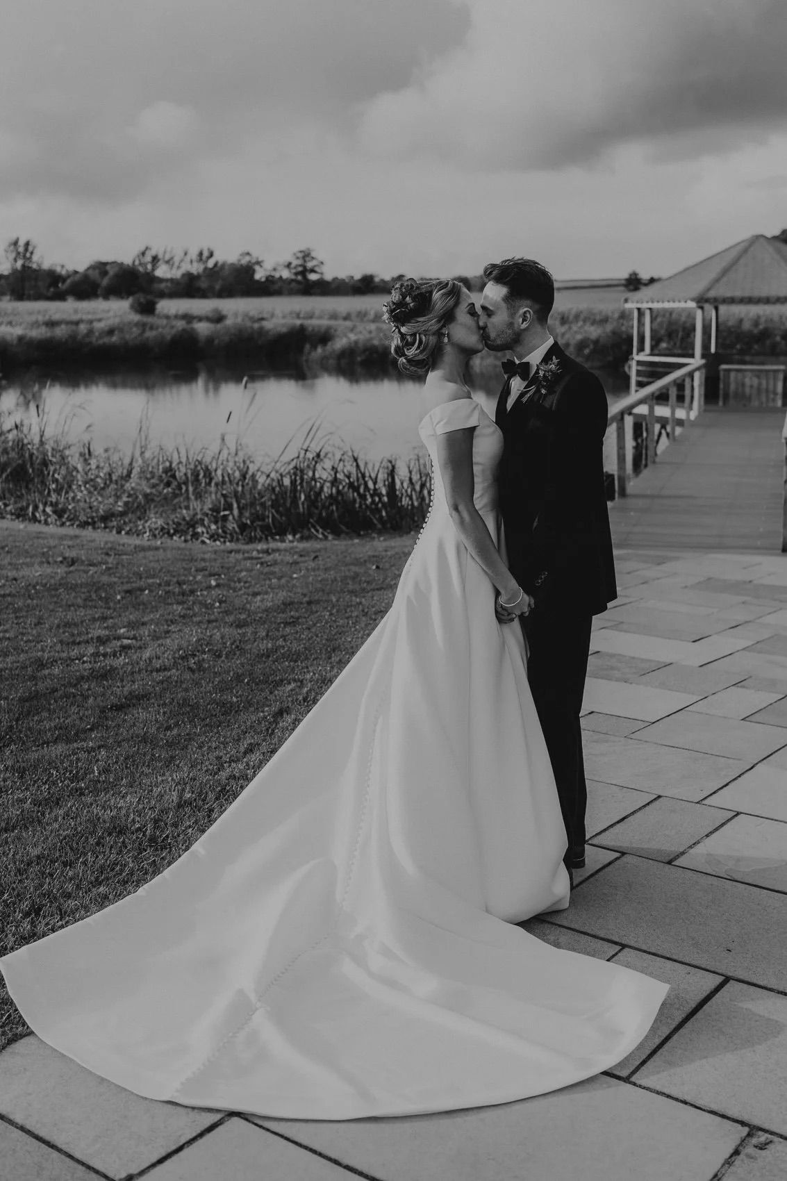 A dramatic black and white photo of a bride's flowing train on stone patio with cloudy sky.