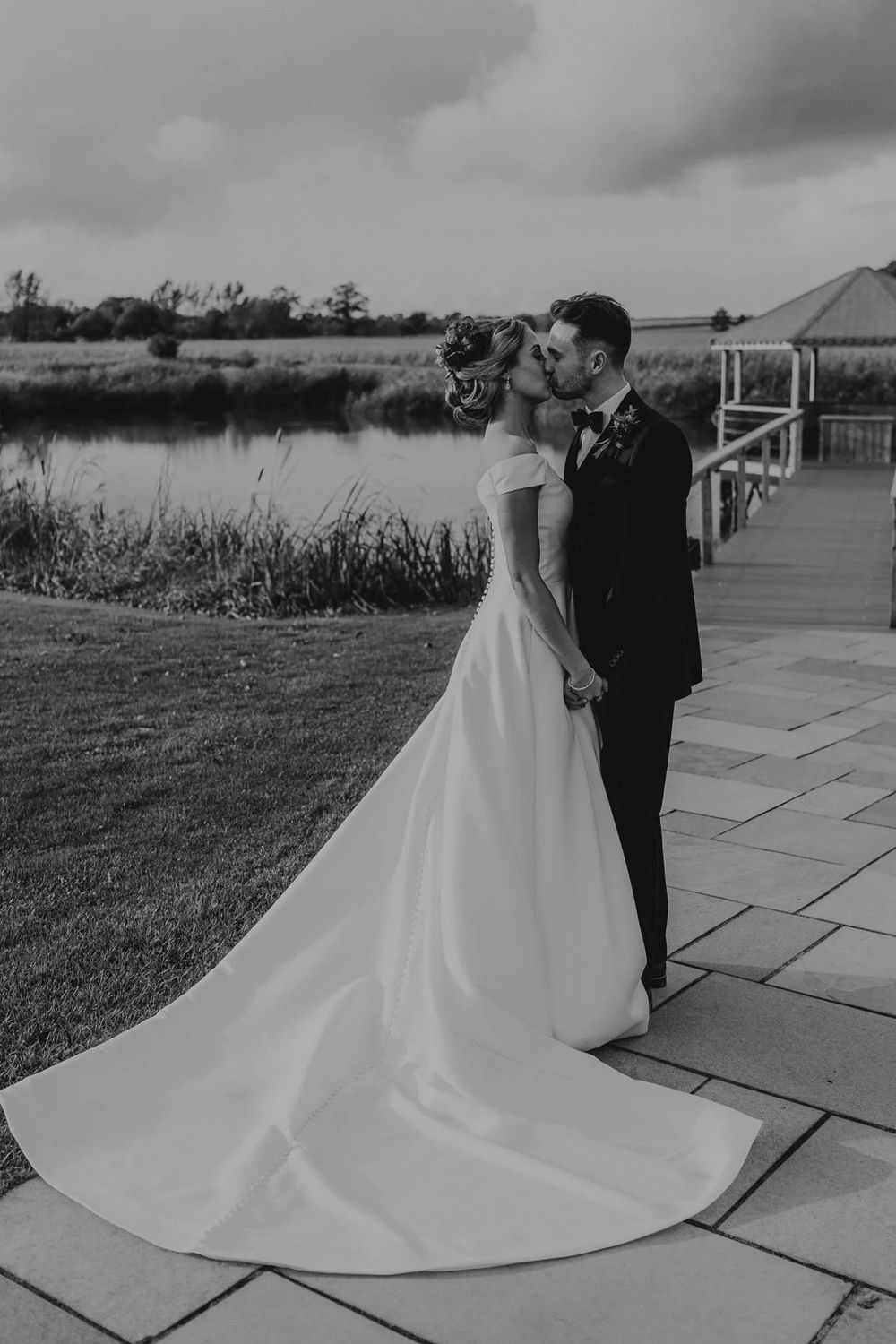 A dramatic black and white photo of a bride's flowing train on stone patio with cloudy sky.