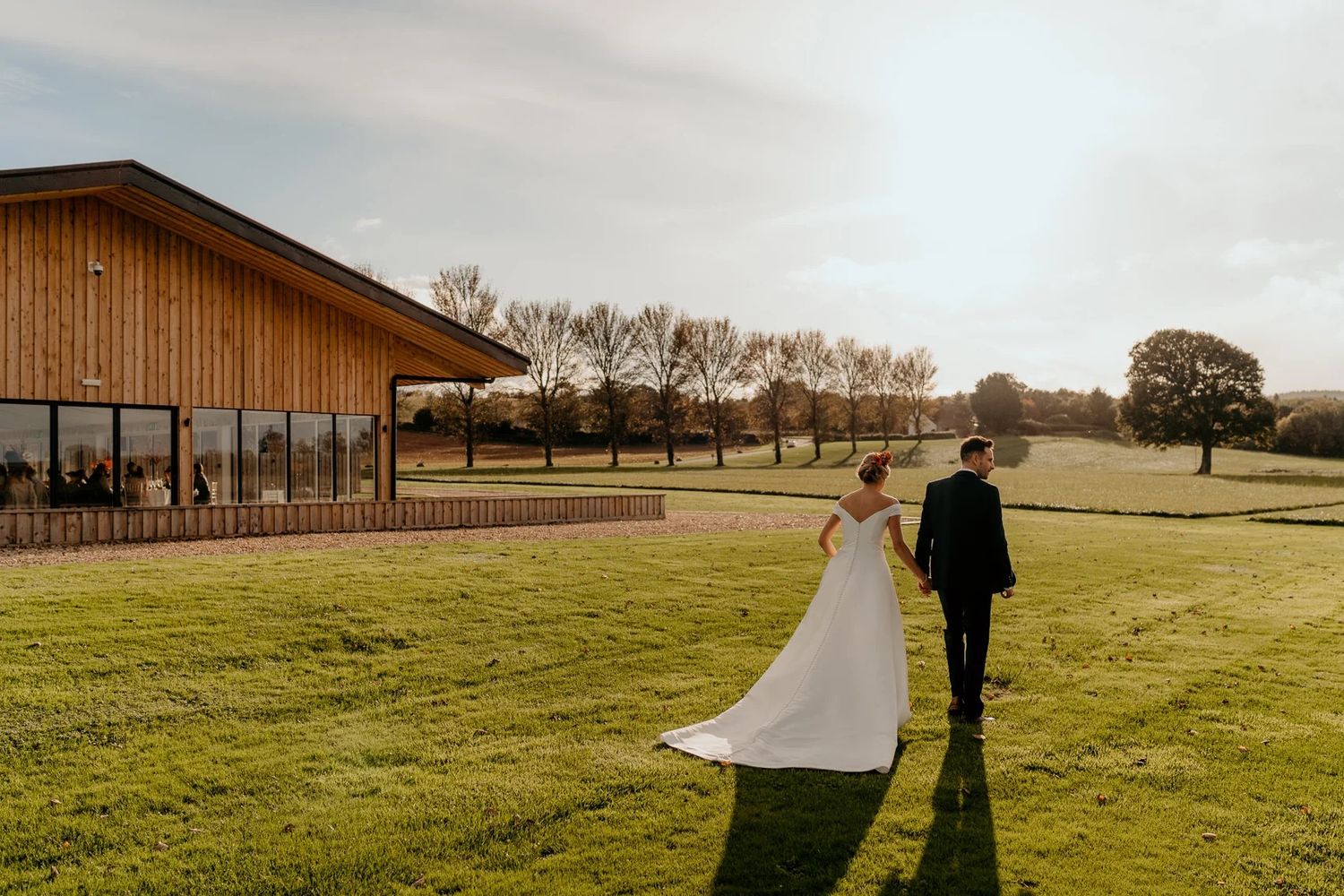 A rural wedding venue displays a panoramic view of rolling green fields and a rustic barn structure at sunset.