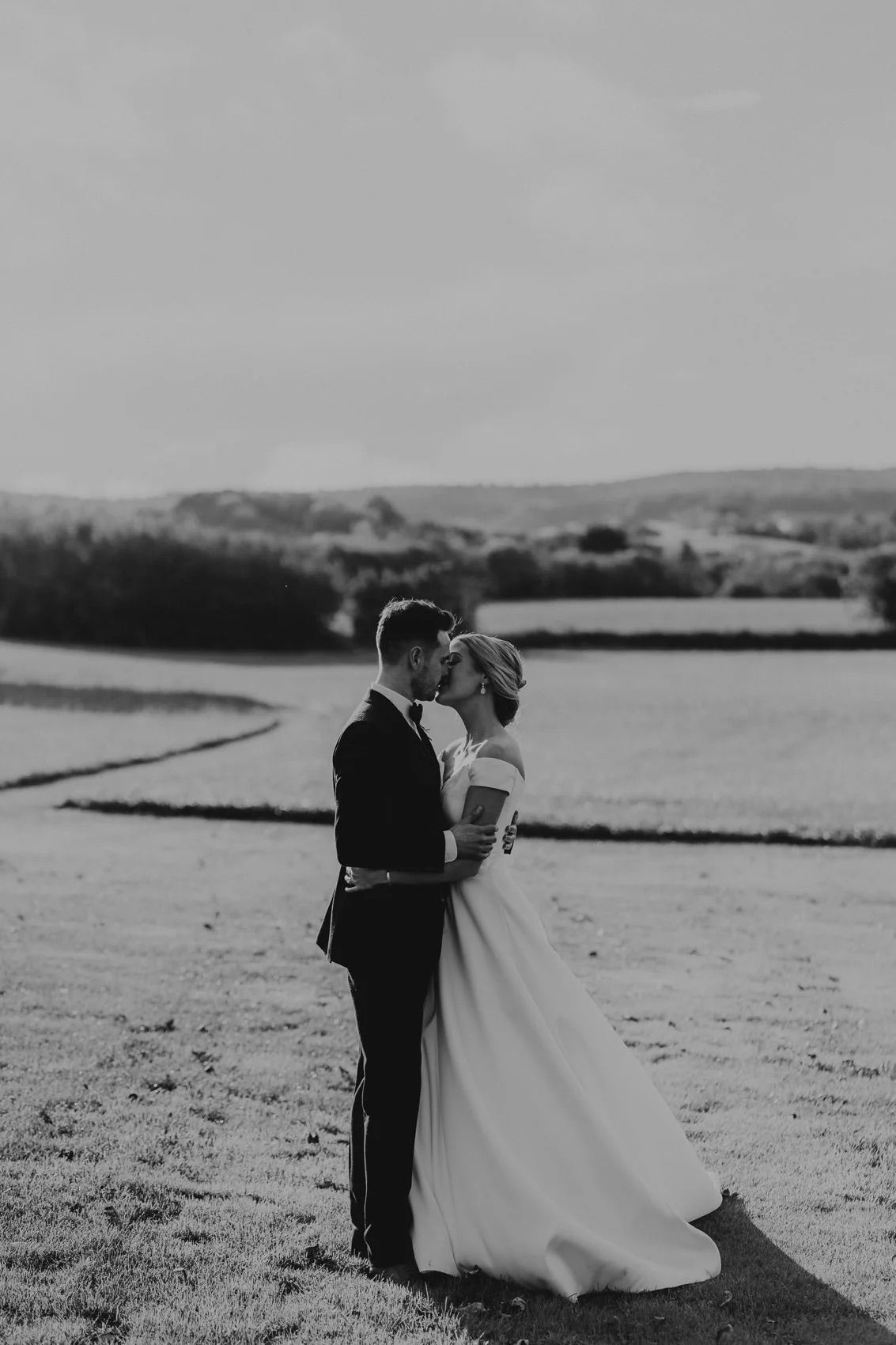 Black and white wedding portraits of couple embracing in scenic field setting.