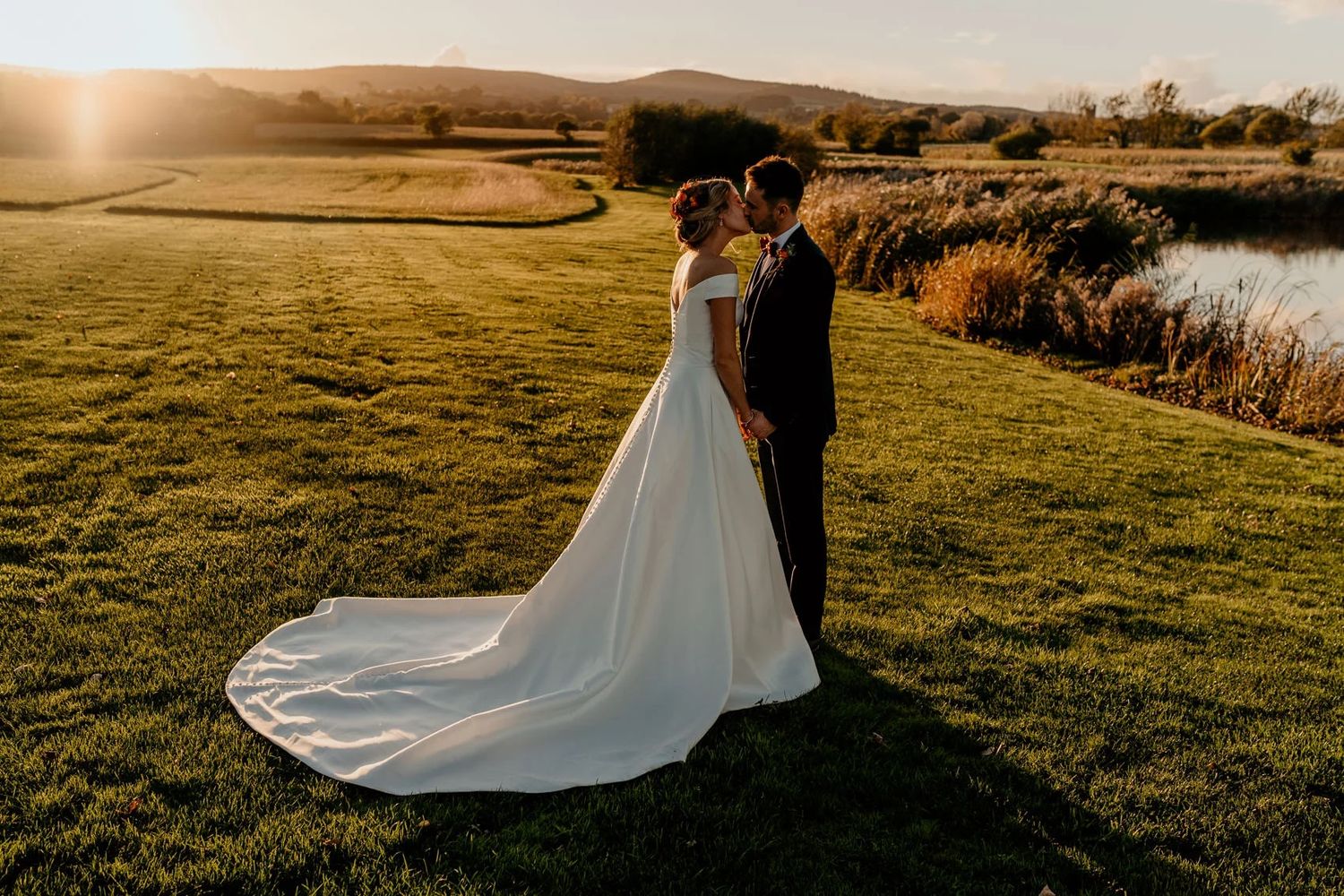 Wedding couple silhouetted against golden sunset light in a scenic countryside field.