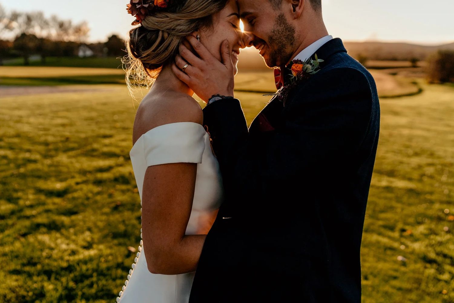 Romantic sunset wedding portrait with golden light filtering through pastoral landscape.