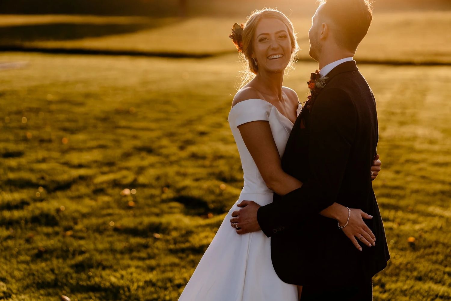 Intimate wedding portrait captured in warm golden hour light across grassy field.