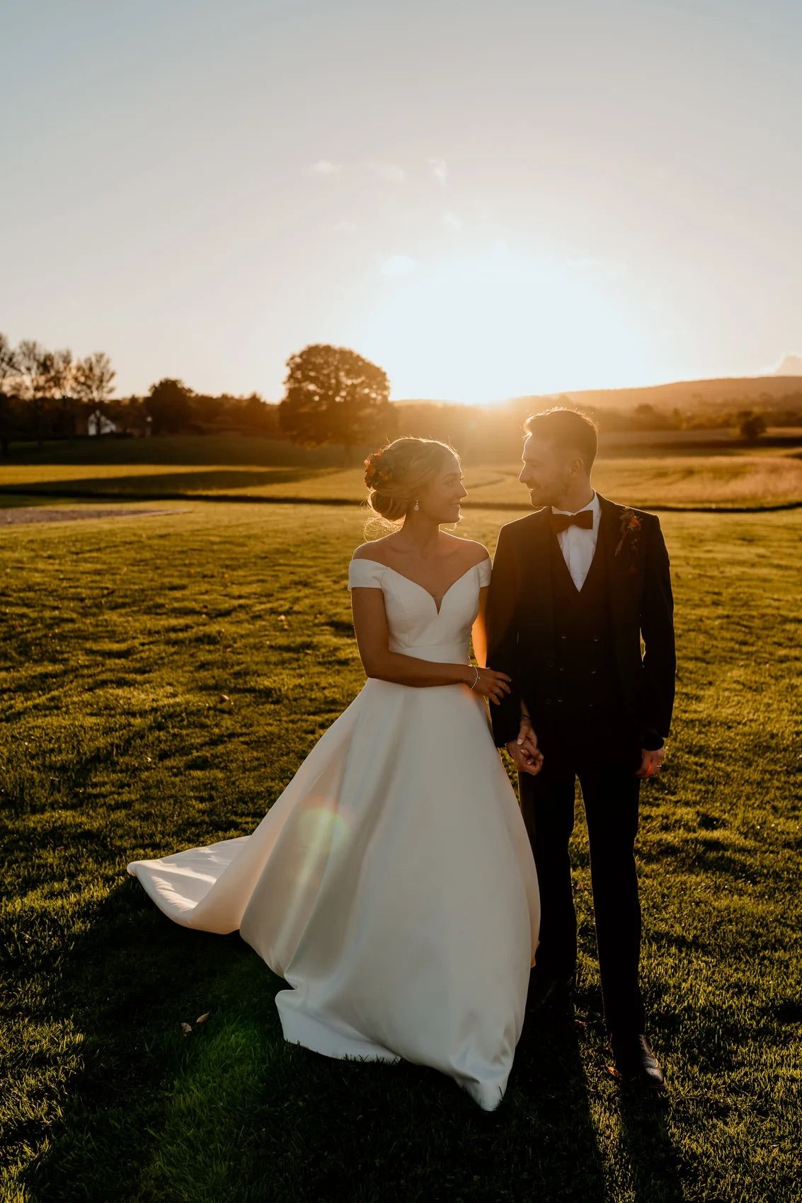Romantic sunset photo session with couple walking through sunlit meadow in wedding attire.