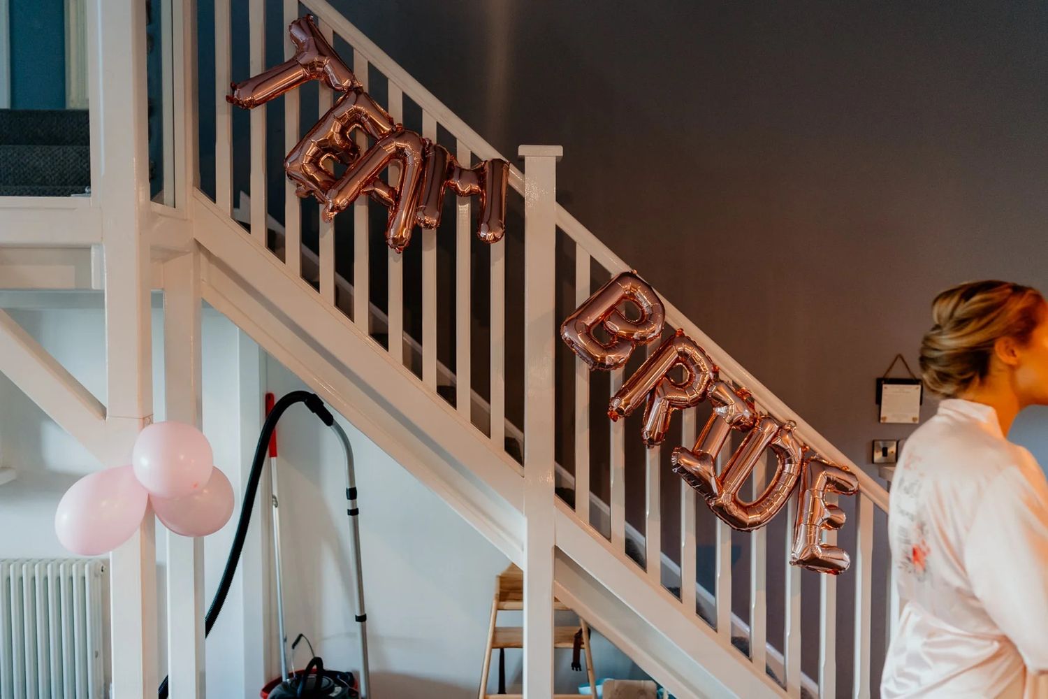 White staircase railing decorated with diagonal gold letter balloons and pink balloons for party decor.