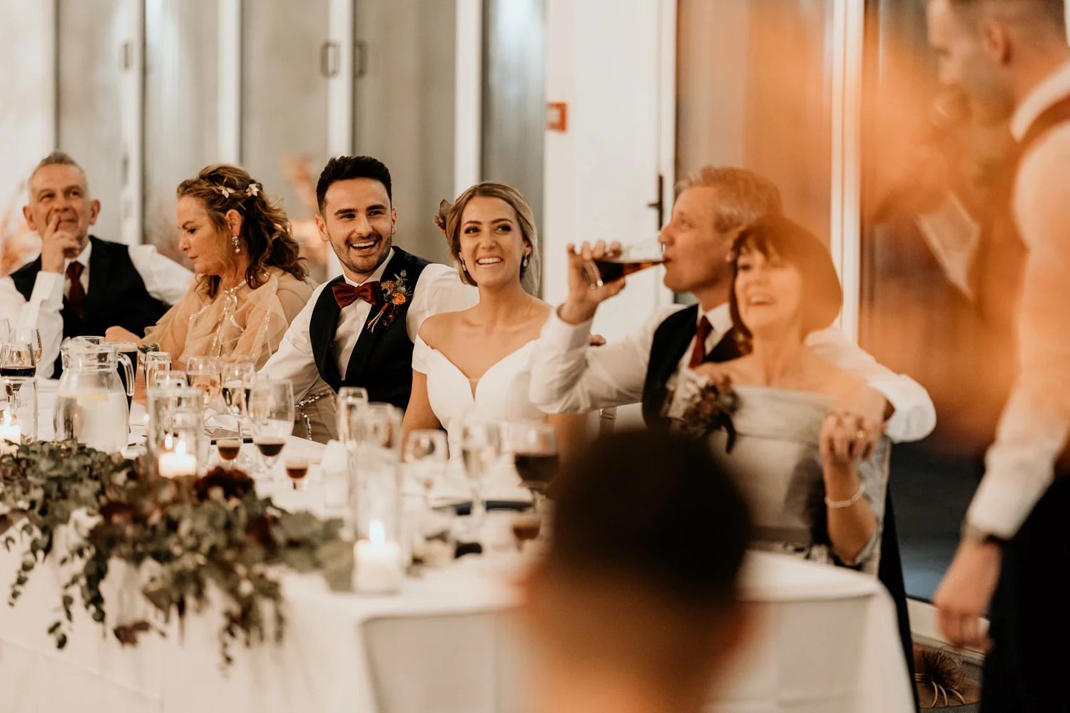 Wedding reception party guests dancing and celebrating in warm ambient lighting.