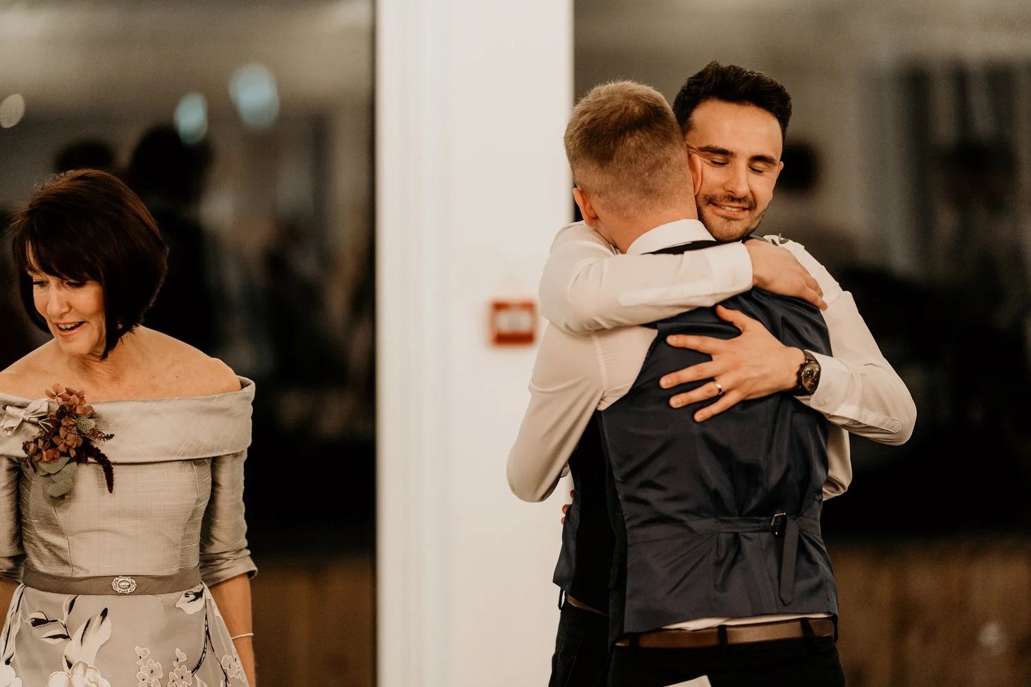 Emotional wedding reception moment with guests embracing in warm indoor lighting.