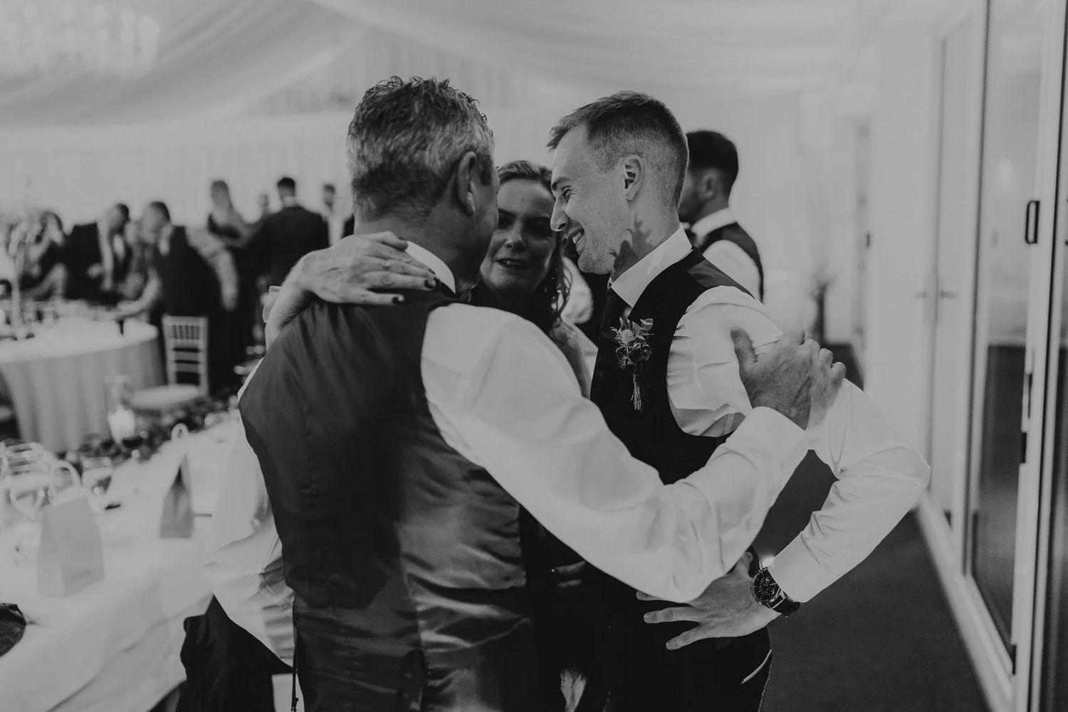 Black and white candid shot of wedding guests sharing emotional moment at reception.