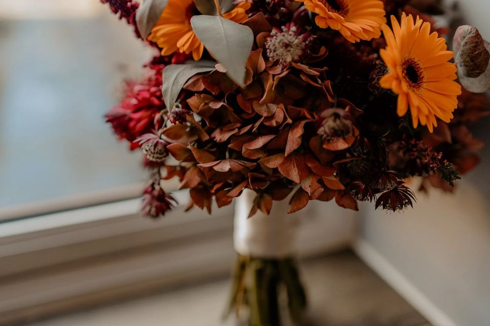 Orange and pink flower arrangements in vases line a window sill with sunlight streaming through.