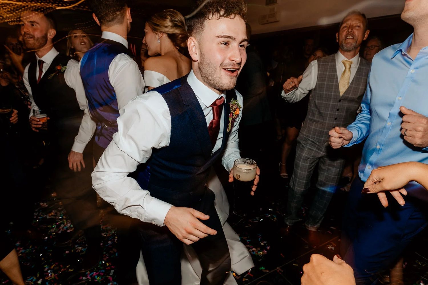 Wedding guests dance and celebrate on a crowded dance floor at an evening reception.