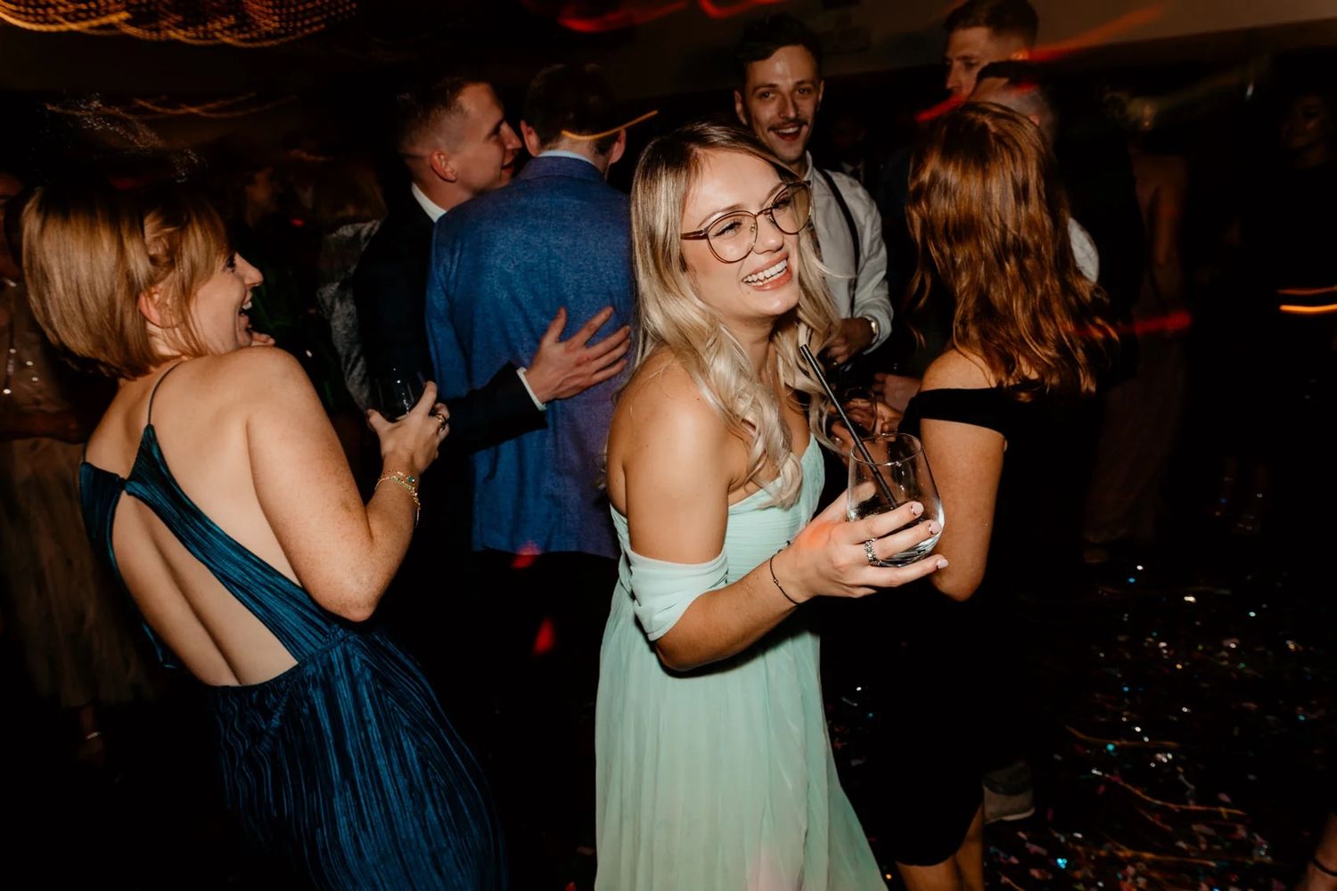 Guests celebrate and dance together on a dimly lit dance floor at an evening reception.