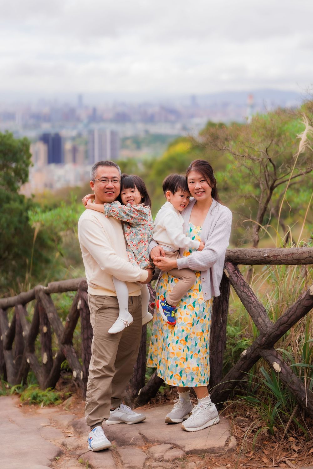 Family enjoying a tender moment together while climbing the steps to Junjianyan hiking trail with Taipei City background