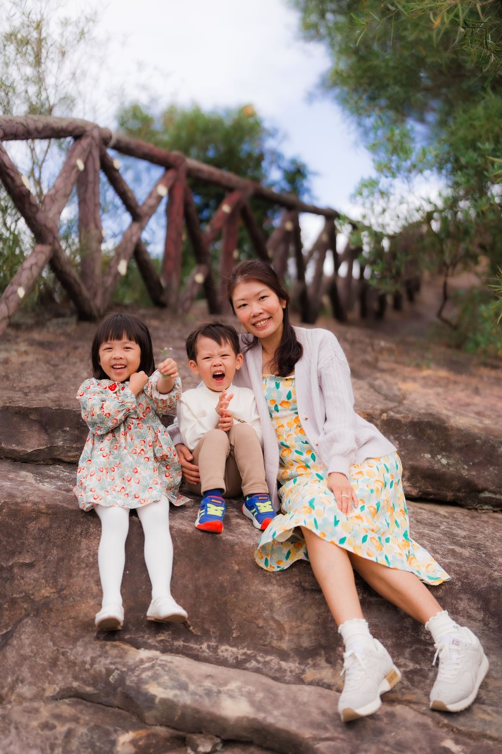 A joyful moment of a mother and two children sitting on Junjianyan hiking trail stairs on a sunny day.