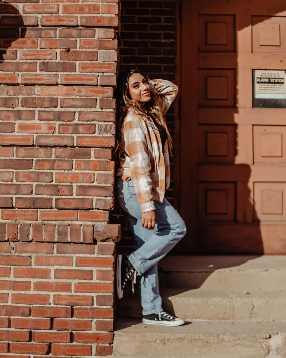 Urban fashion photoshoot featuring casual style against red brick wall and brown doorway in natural lighting.