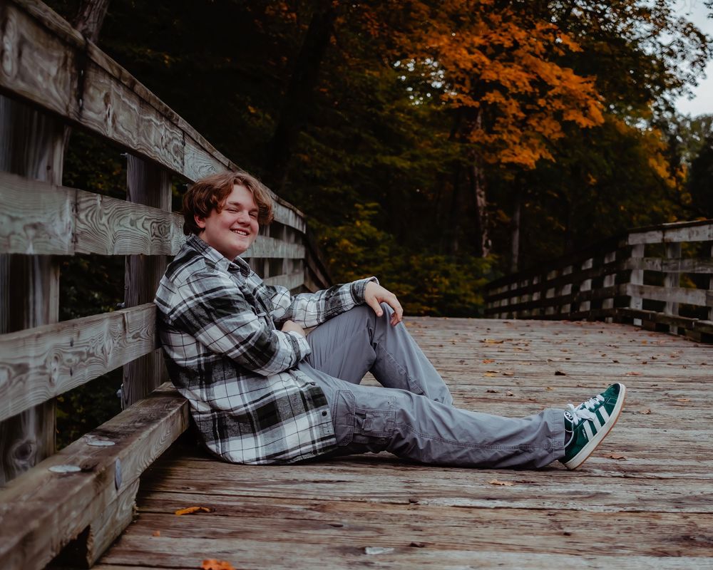 Person lying on a wooden bridge deck in autumn with fallen leaves scattered around.