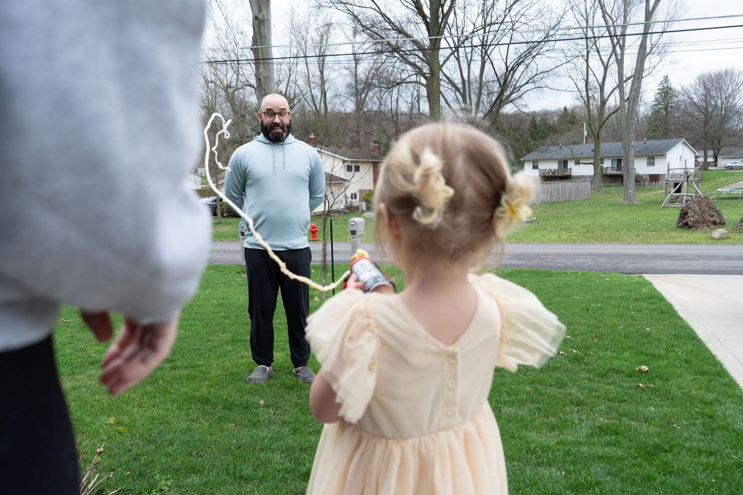 Children play energetically with bubbles in a grassy backyard during springtime outdoor activities.