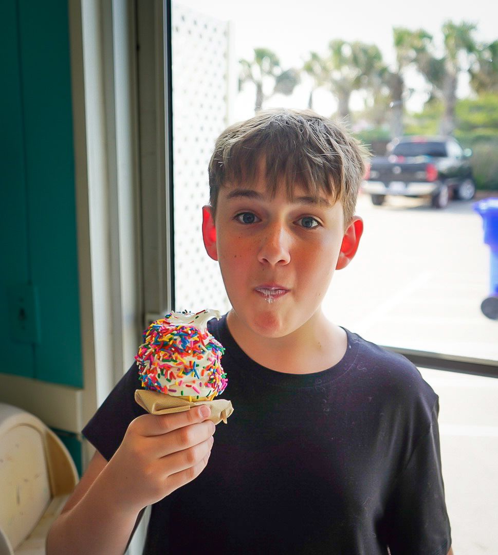 Someone enjoying a rainbow sprinkle ice cream cone by a window on a sunny day.