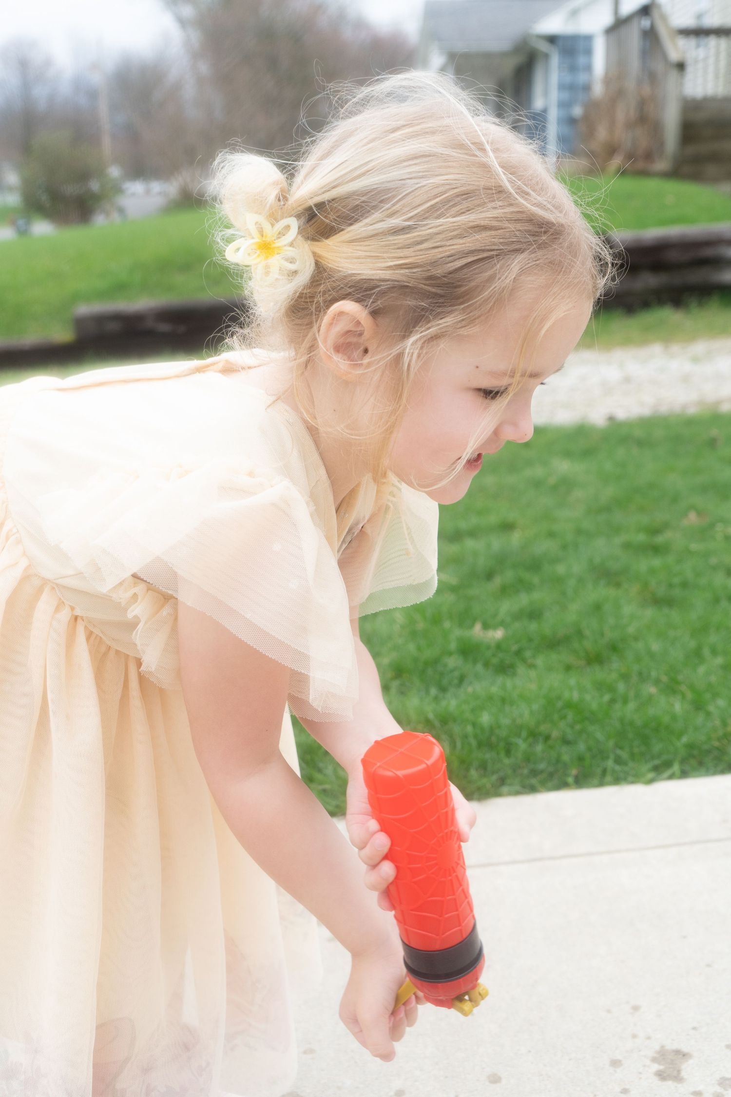A person in a cream-colored dress holds red cups while bending down in a grassy outdoor setting.