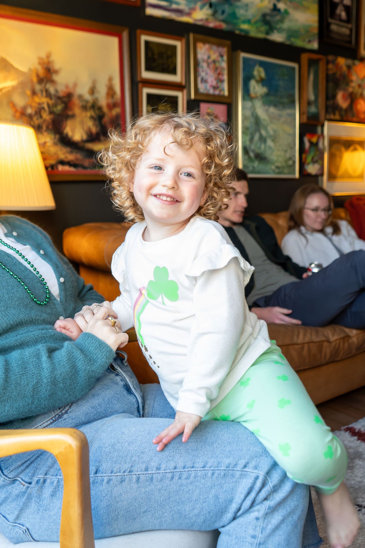 A playful toddler laughs while sitting on a couch in a room decorated with framed artwork on the walls.