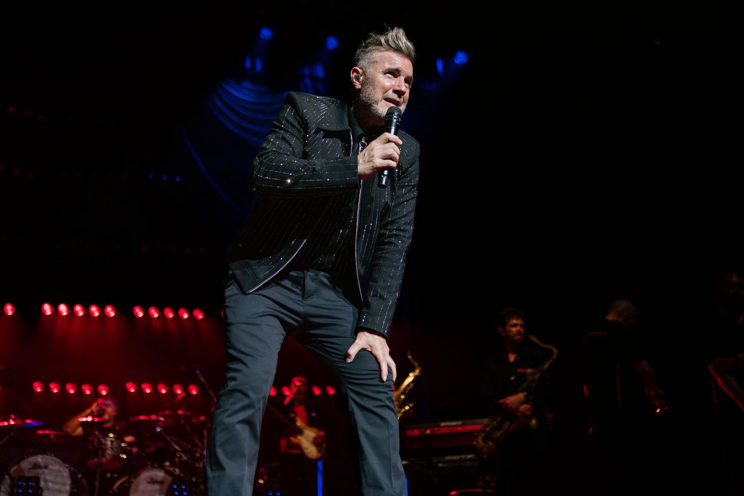 Singer performing live on a dimly lit stage with dramatic red and blue lighting effects.