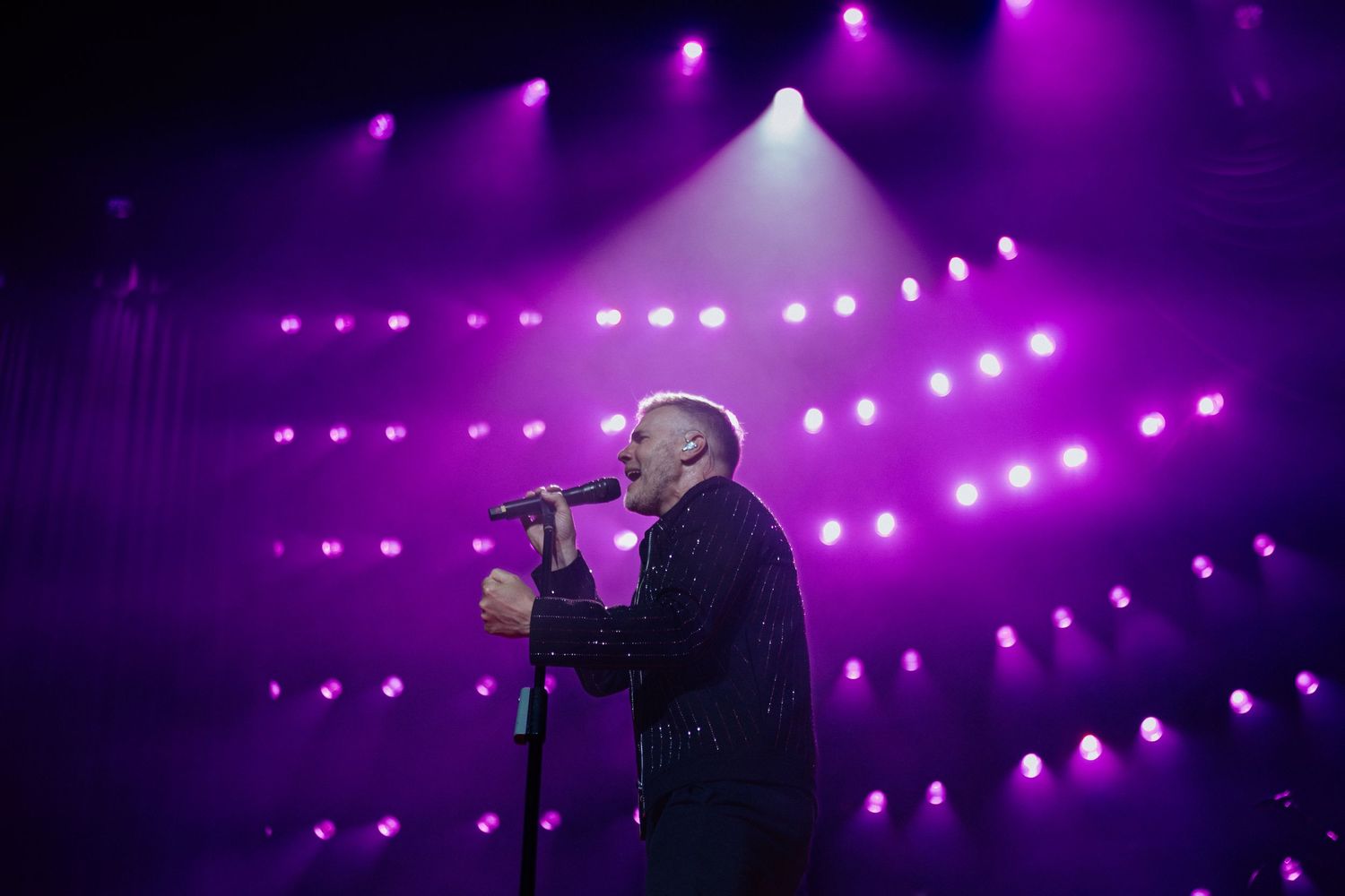 A silhouetted singer performs on stage against a backdrop of purple lighting and glowing orbs.