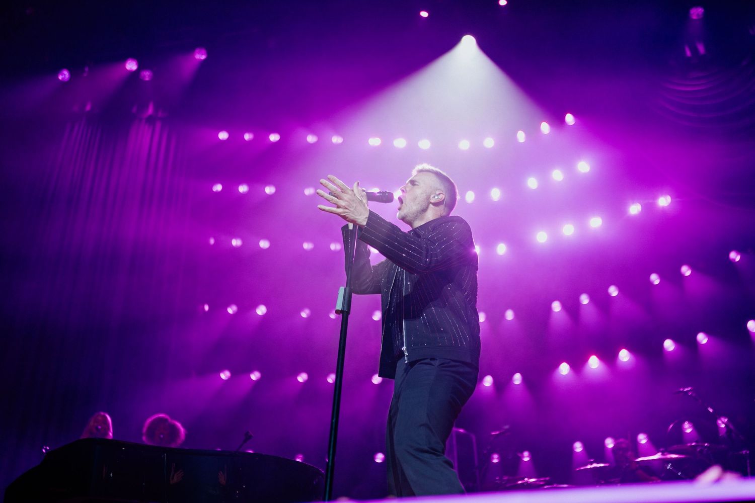 Concert performer singing on stage with dramatic purple lighting and string lights creating an atmospheric effect.