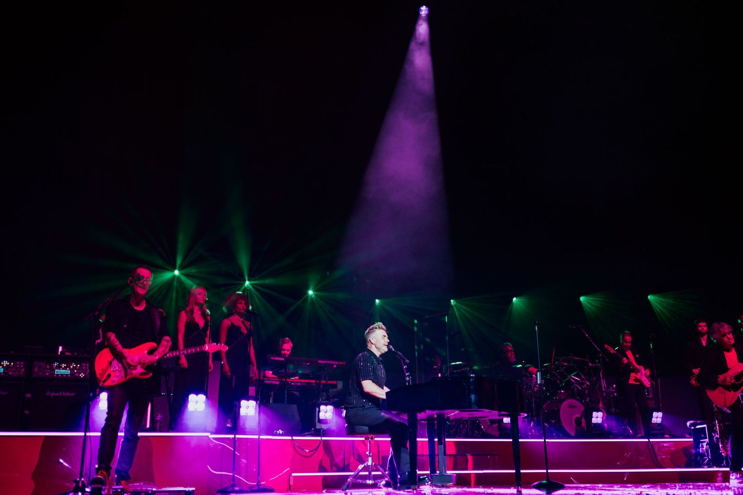 Concert stage illuminated with vibrant purple and red lighting during a live musical performance.