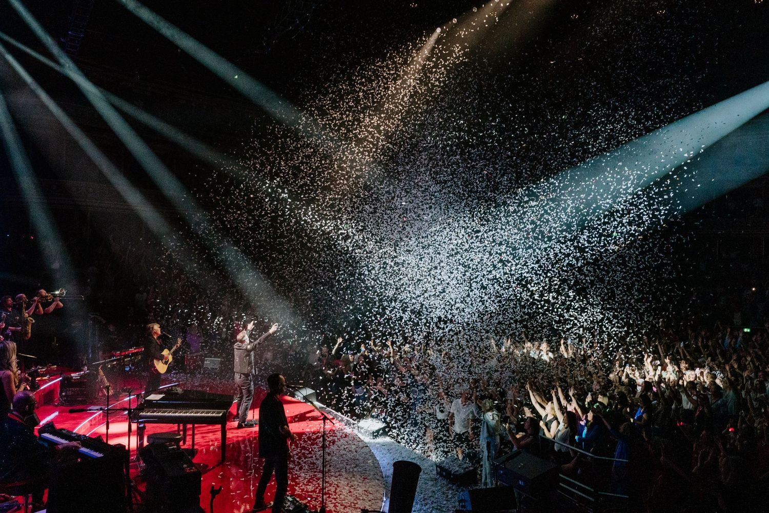 Concert arena filled with swirling white spotlights and fog effects creating a dramatic atmosphere above crowd.