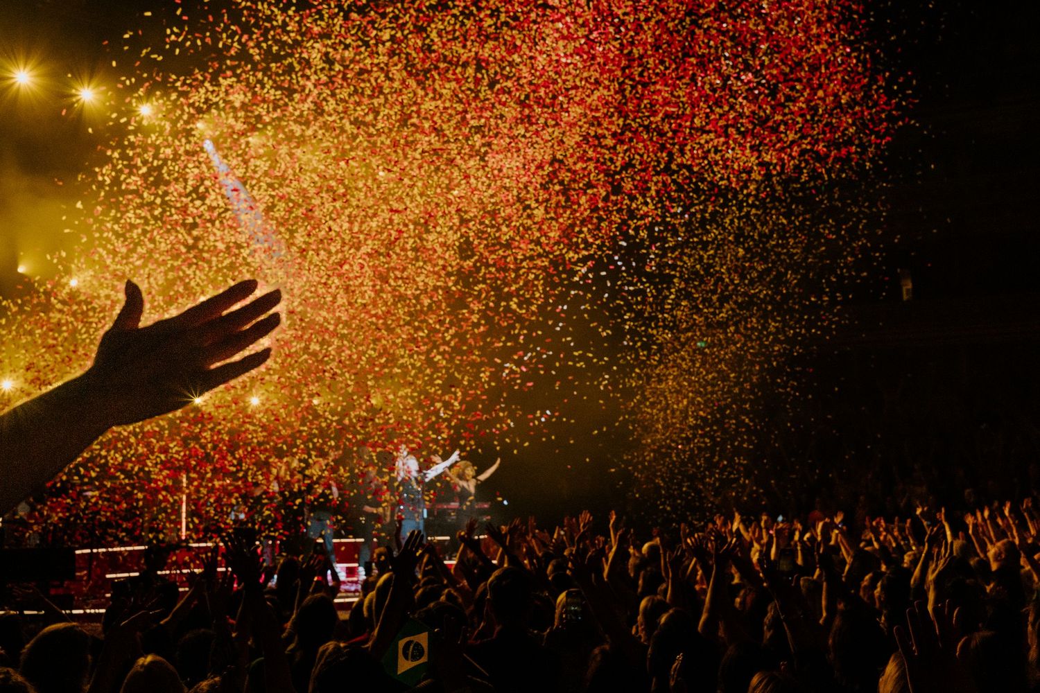 Golden confetti rains down over silhouetted concert crowd during nighttime performance.