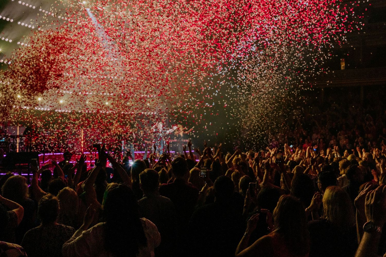 Red confetti shower fills concert venue as crowd cheers during performance.