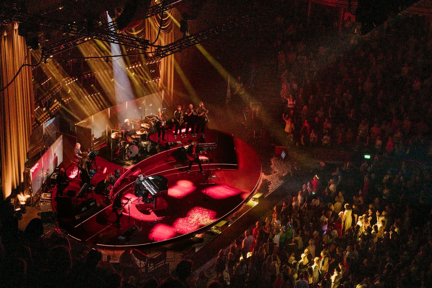 Concert venue illuminated with dramatic red lighting and smoke effects during live performance.