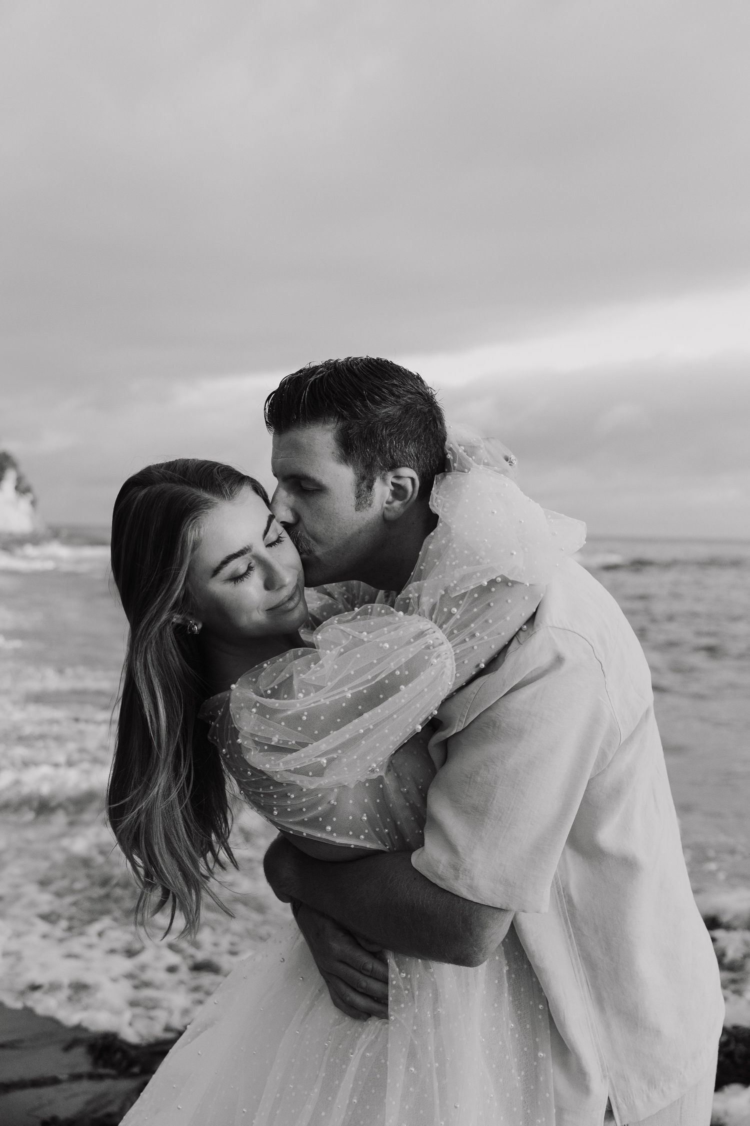 Black and white beach photography series showing romantic couple wrapped in flowing fabric.