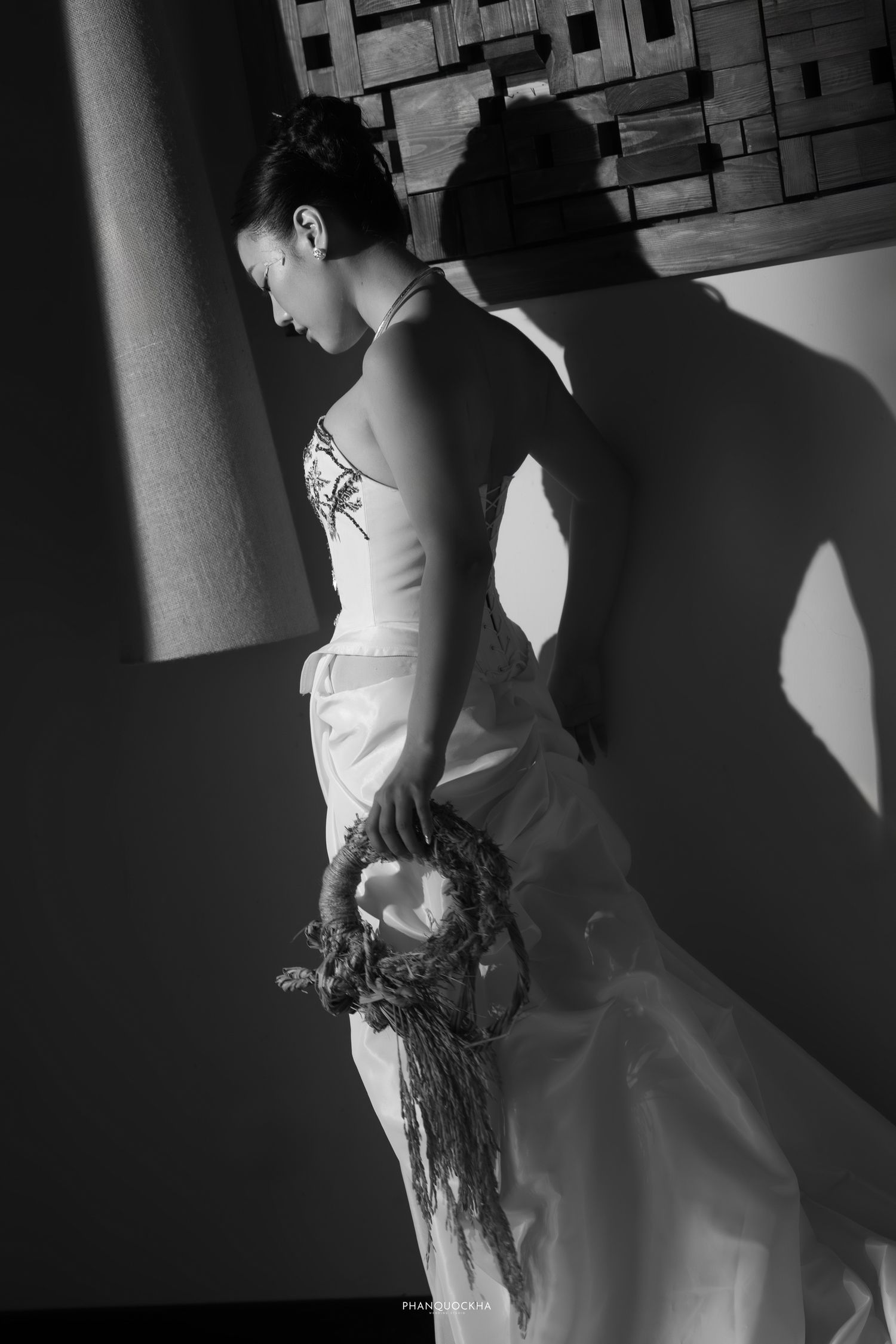 Black and white photo of bride in embroidered gown holding dried wreath bouquet.