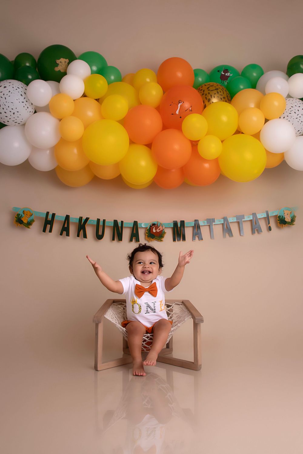 Festive balloon arch in orange, yellow and green with Hakuna Matata banner and small seated figure below.