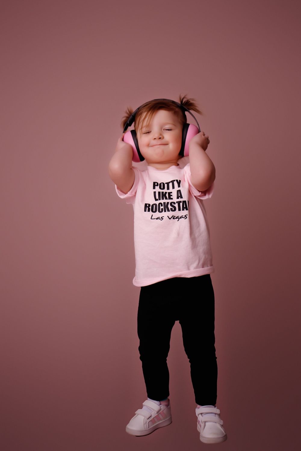 Small child in pink t-shirt and black pants dancing and playing in studio setting with pink backdrop.