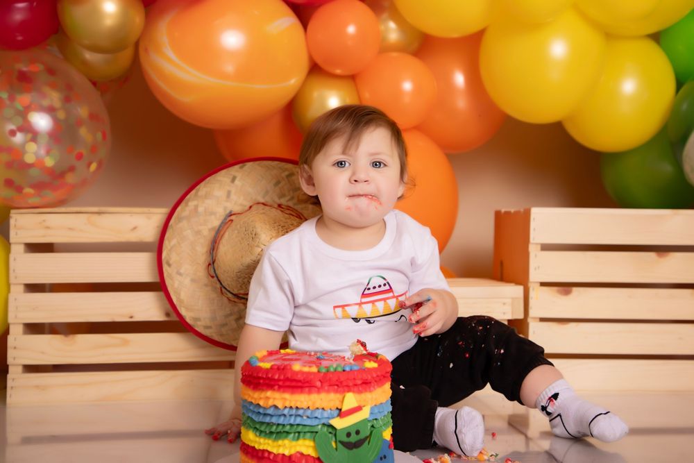 A colorful first birthday party setup with wooden crates, balloons, and a small celebrant in festive attire.