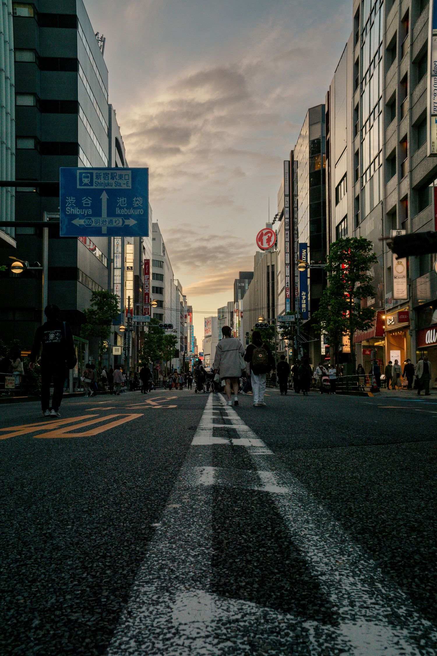 Moody twilight view down a Tokyo street with white road markings and tall buildings against a dramatic sunset sky.