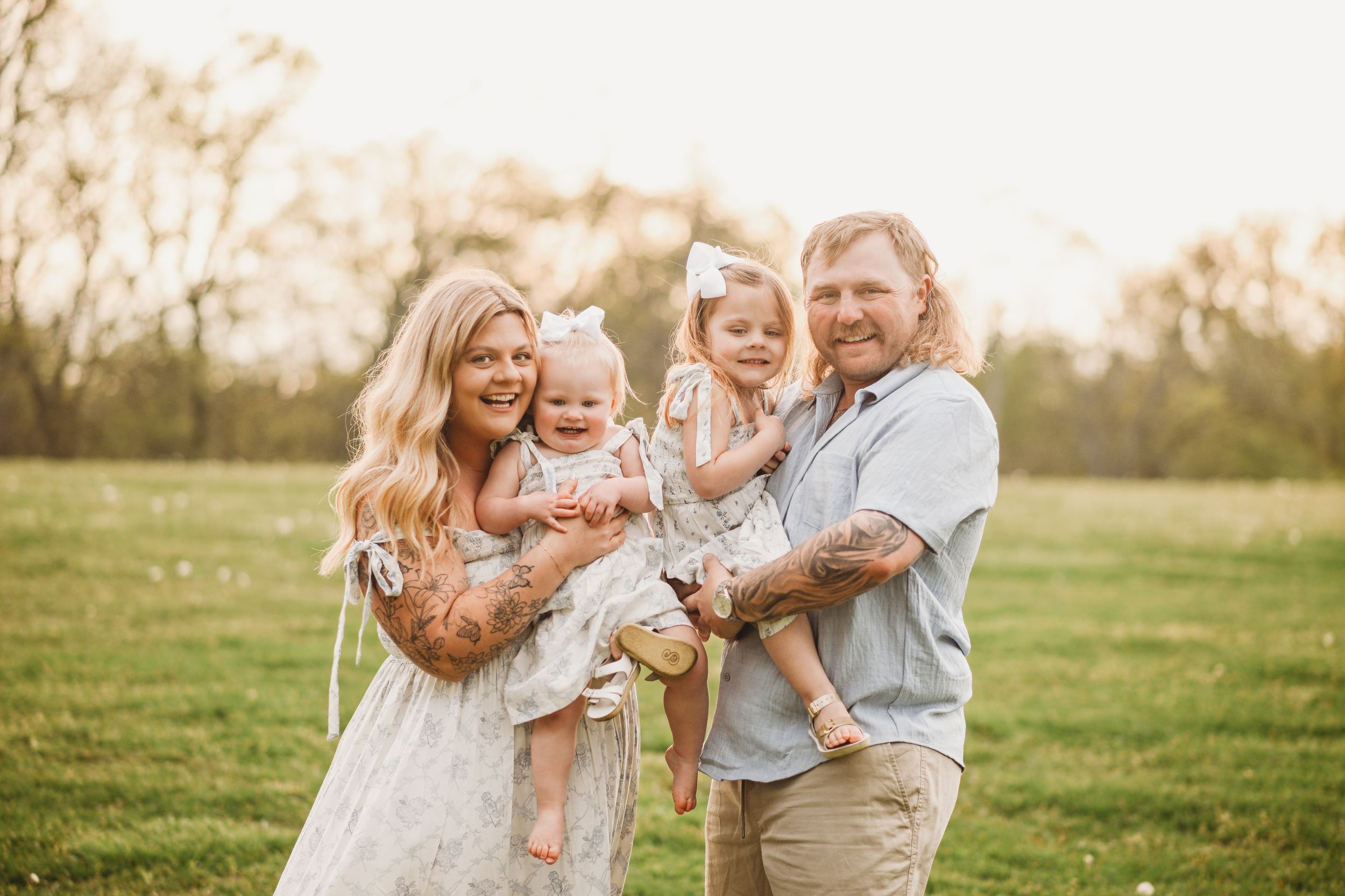 Family members playing and laughing together in an outdoor field at sunset.