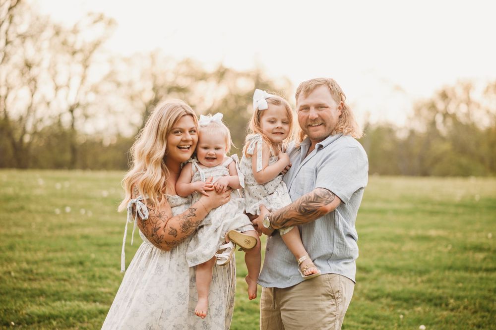 Family members playing and laughing together in an outdoor field at sunset.