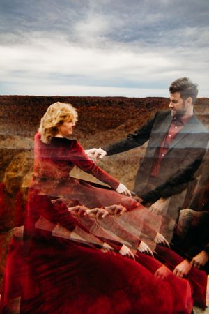 Artistic double exposure photo of couple in red dress and black suit dancing on rocky mountain overlook in autumn.