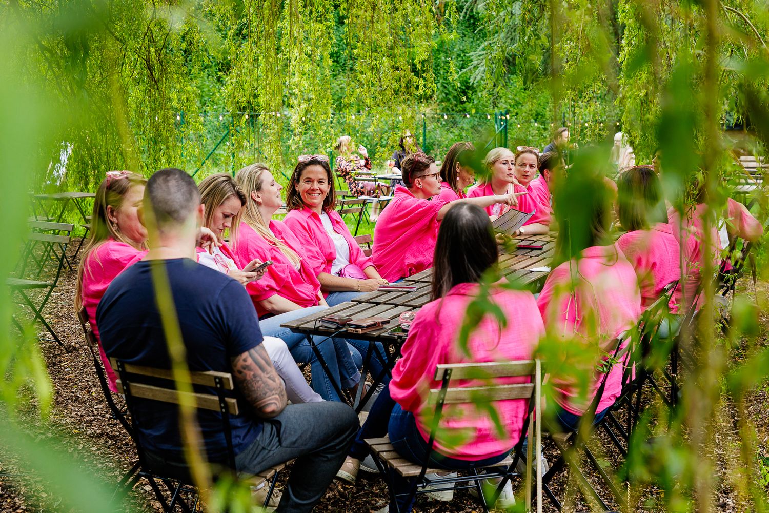 A group gathers for an outdoor activity in a lush green forest setting with pink clothing visible.