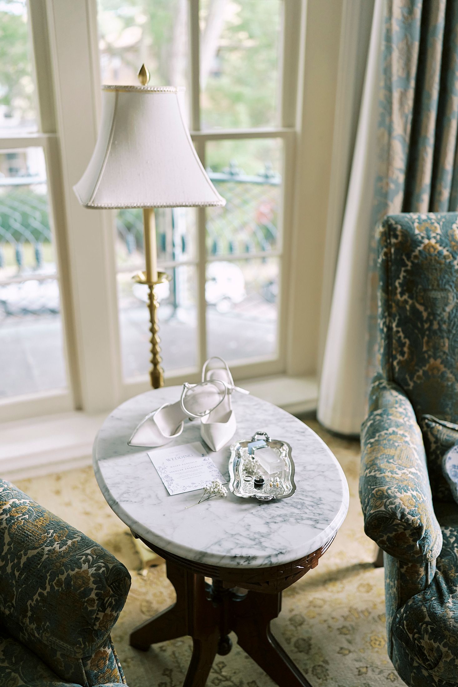 Table lamp on round marble side table with elegant decor details in a sunlit window-filled room.