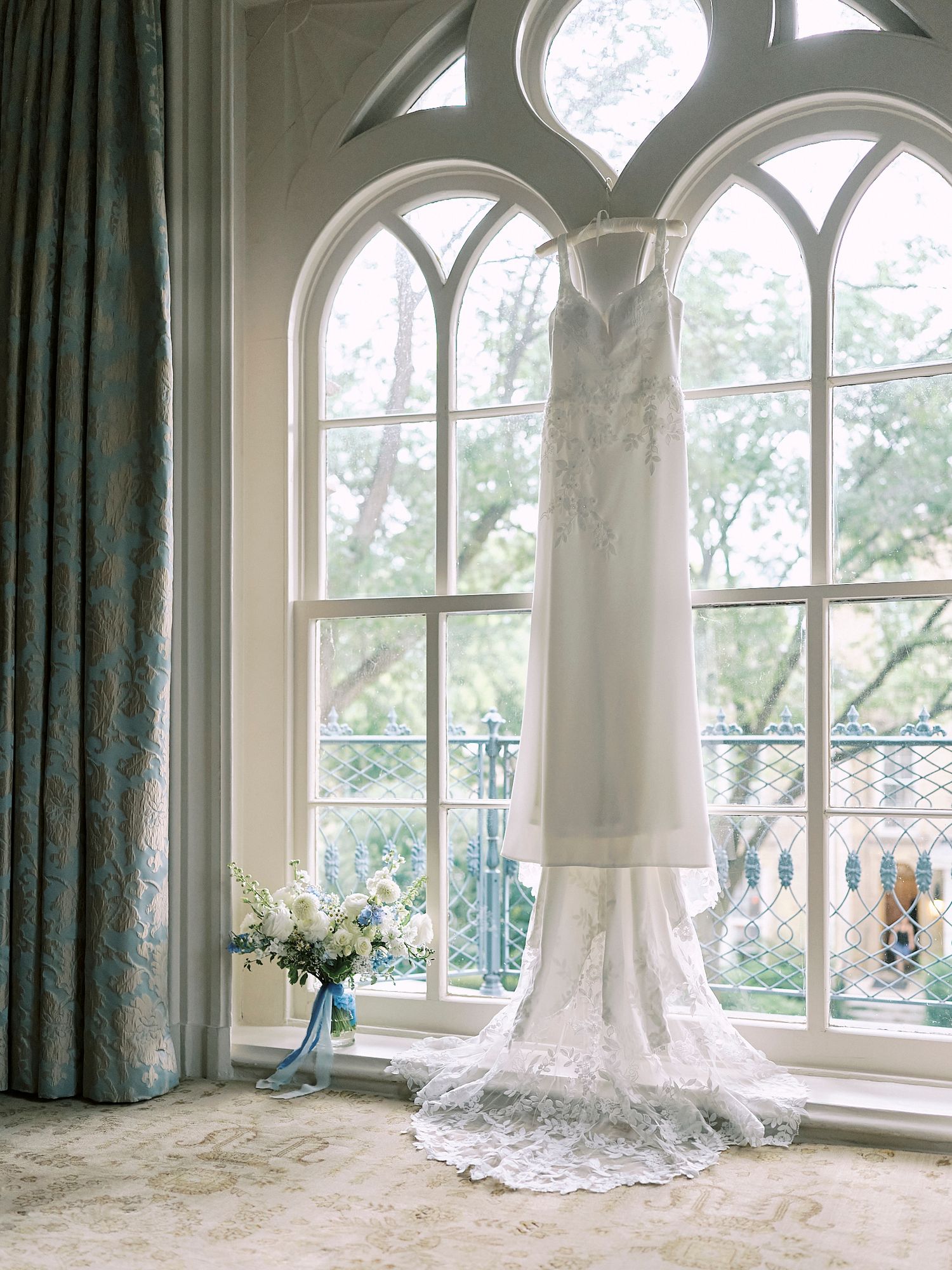 An elegant white wedding dress displayed in front of arched windows with natural light streaming in.