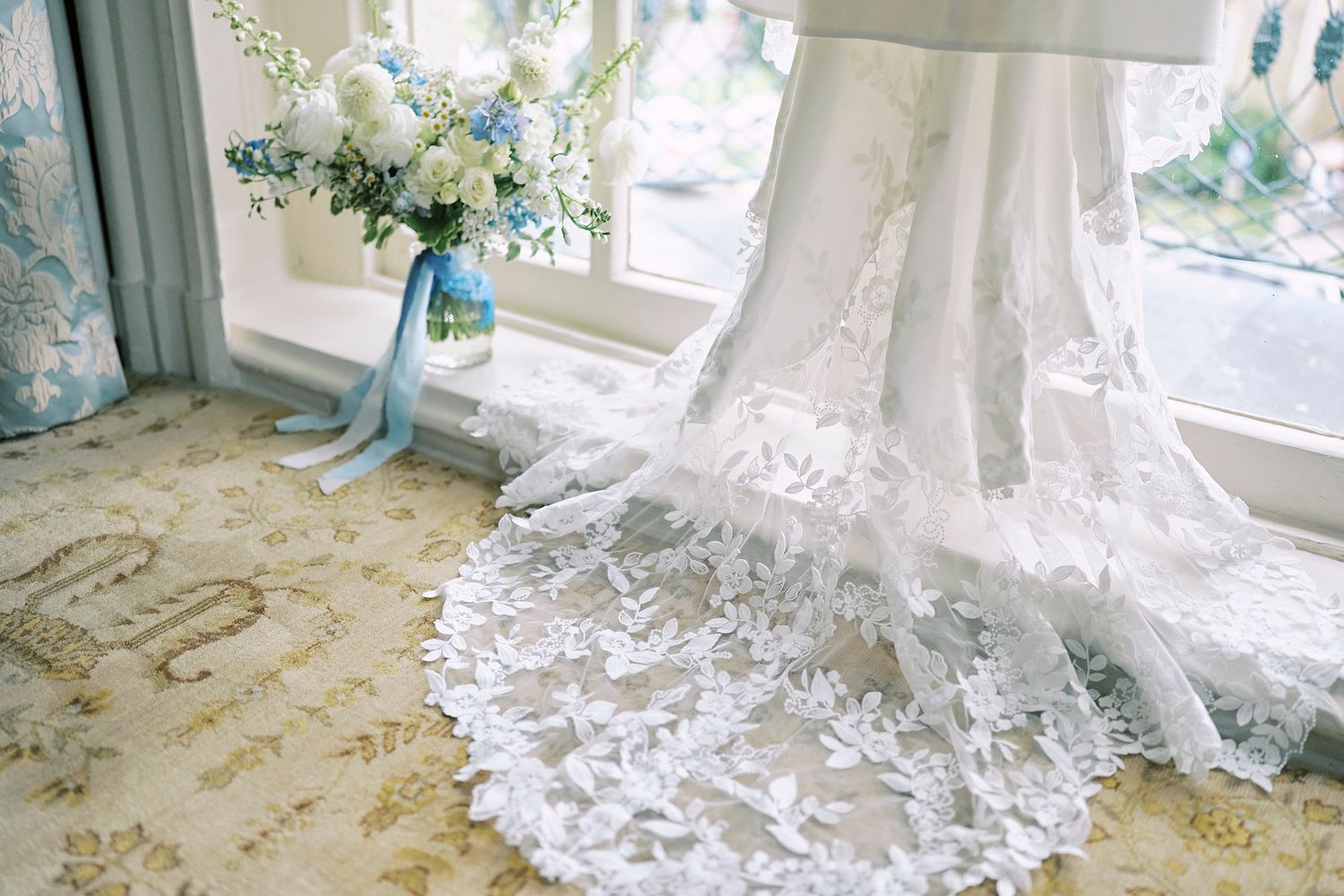 Intricate white lace detail from a wedding dress train laid out on a patterned floor.