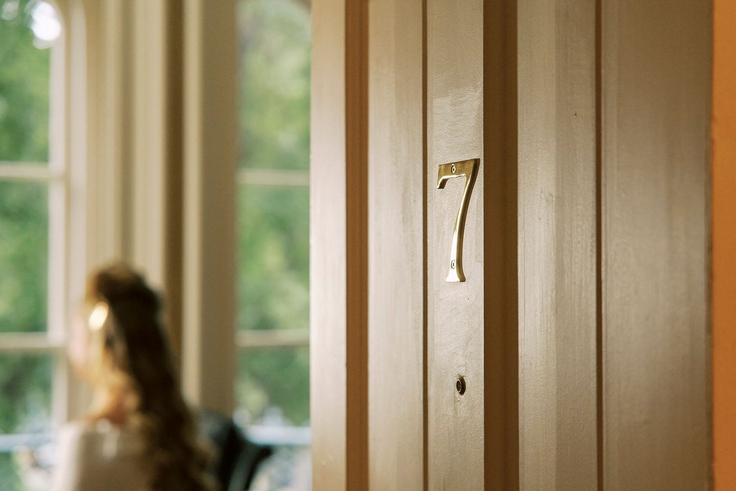 Wooden hallway with numbered doors and sunlight streaming through windows.