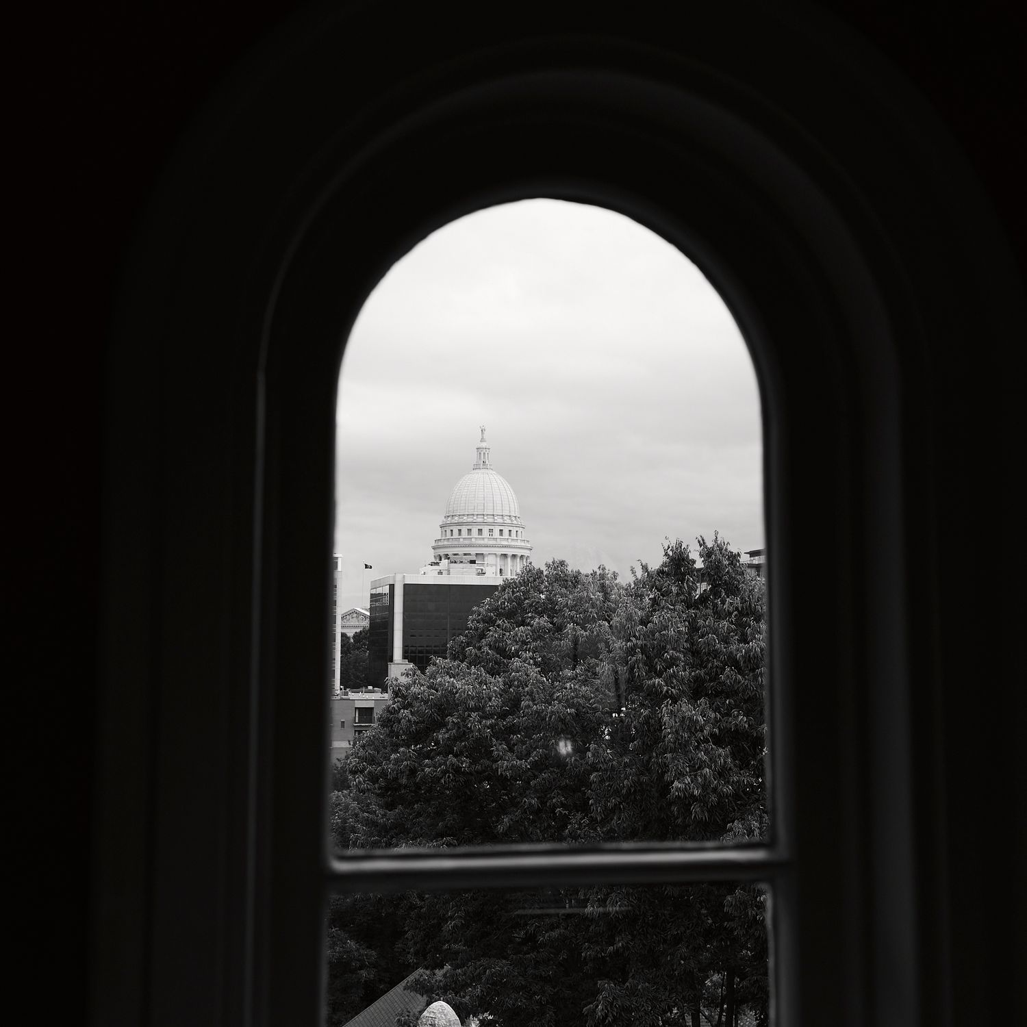 View of a domed government building through an arched window frame in black and white.